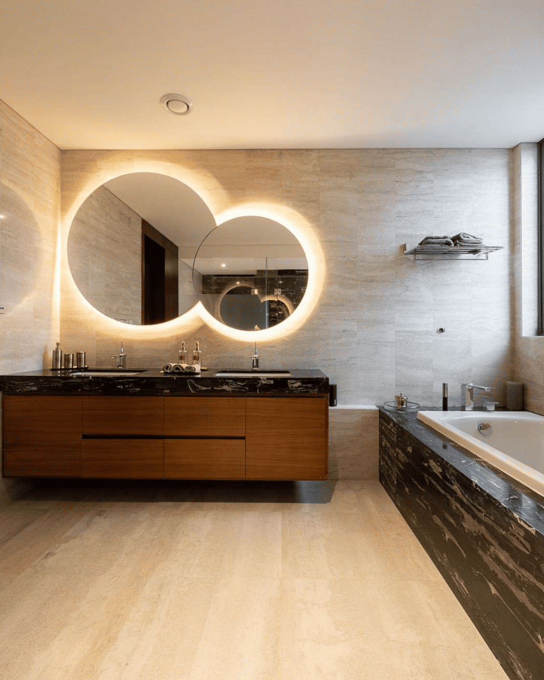 Bathroom with layered circular backlit mirrors and marble tub surround